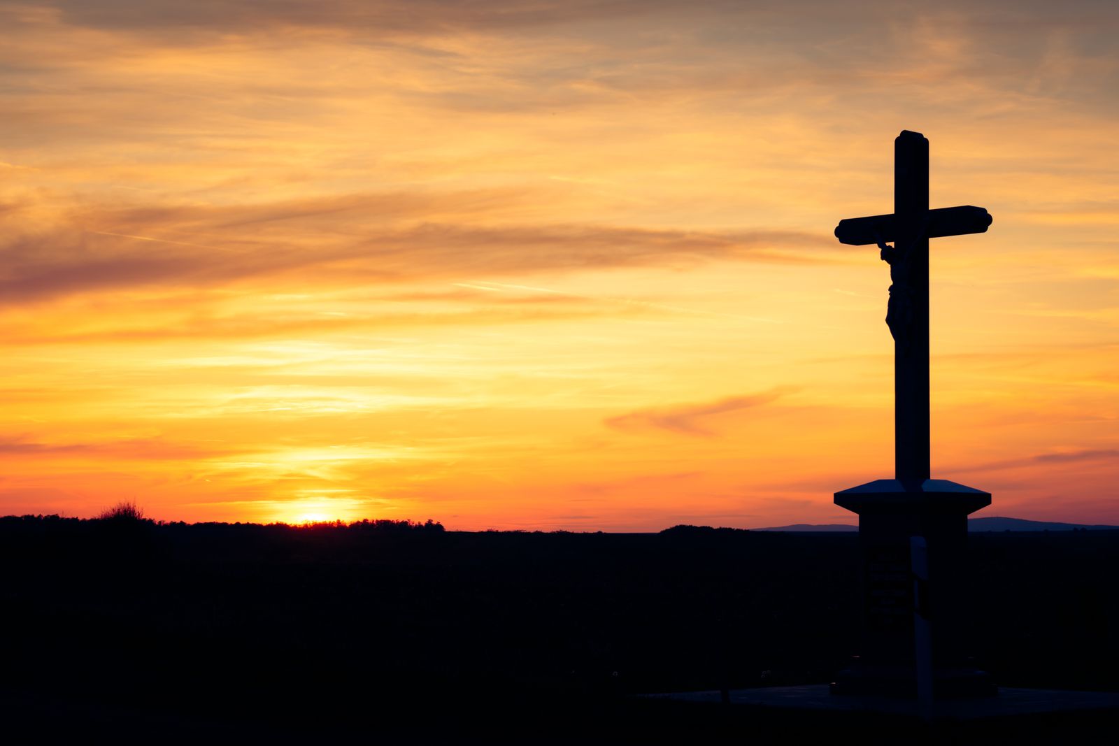 A cross silhouetted against a golden sunrise sky
